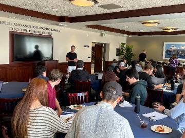 almis standing in front of groups of students sitting at tables