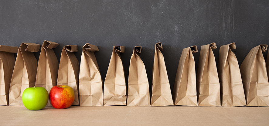 Brown lunch bags in a line with apples in front 