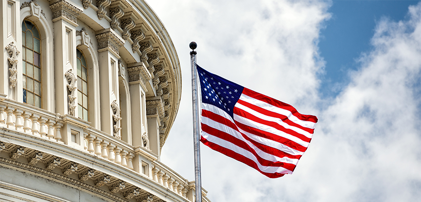 The U.S. Capitol building with an American flag waving against a partly cloudy sky.