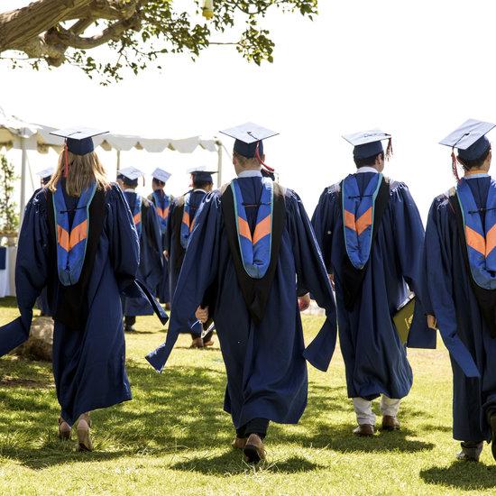 Four students walking on grass at graduation with graduation regalia